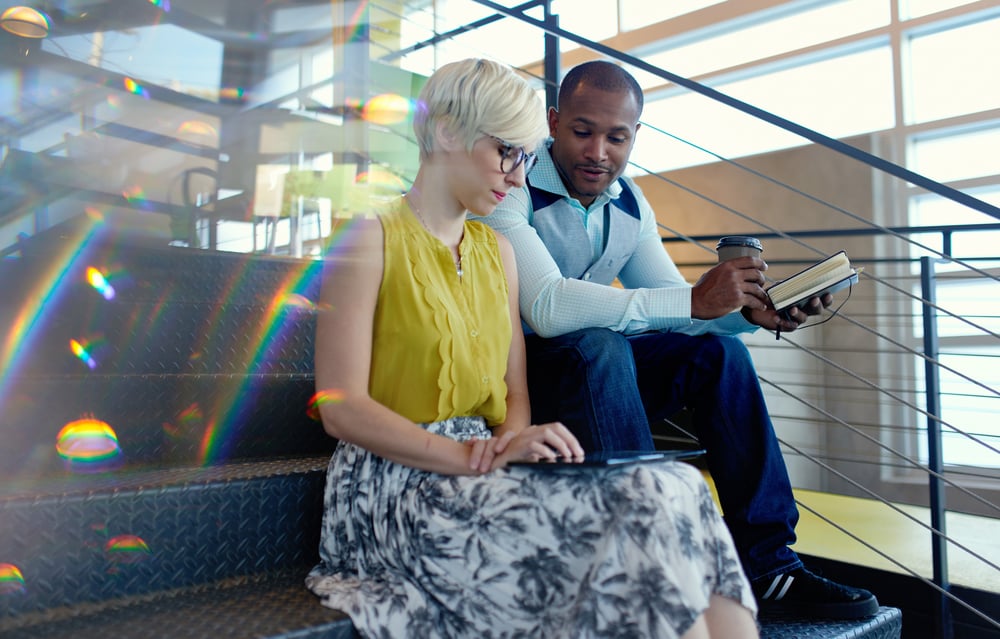 Two creative millenial small business owners working on social media strategy using a digital tablet while sitting in staircase-3